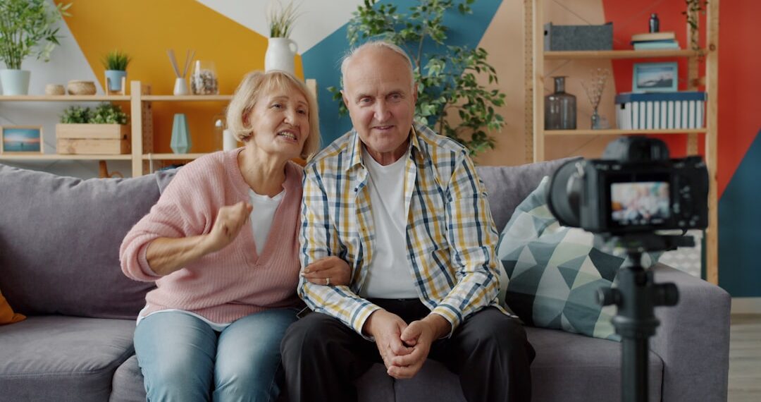 Senior bloggers man and woman are recording video showing thumbs-up using camera at home making content for internet vlog. People and technology concept.