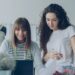 Cheerful creative clothing designers are watching laptop screen, having friendly conversation, gesturing, smiling and laughing together in light workshop. Fun at workplace concept.